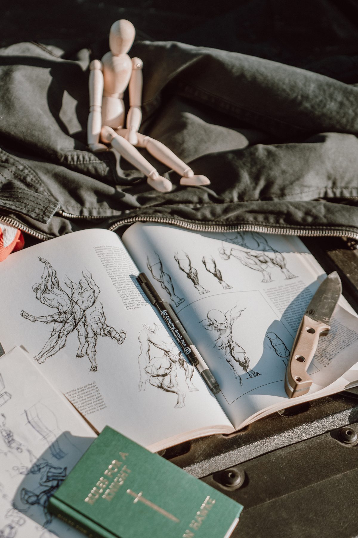 Wooden mannequin on jacket beside open anatomy sketchbook